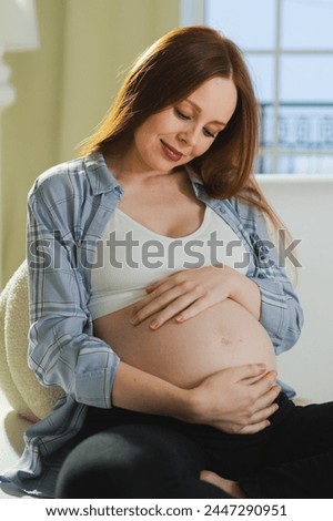 Pregnancy motherhood people expectation future. Pregnant woman touching big belly sitting on couch at home. Girl hugging her tummy enjoying pregnancy. Maternity tenderness parenthood new life concept Royalty-Free Stock Photo #2447290951