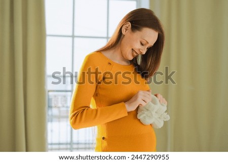 Pregnancy motherhood people expectation future. Pregnant woman with big belly holding newborn baby booties smiling at home. Young mom enjoying pregnancy. Maternity tenderness parenthood new life Royalty-Free Stock Photo #2447290955