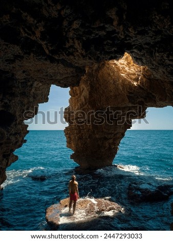 Man illuminated by the sun's rays in the Cueva de los Arcos, with the sea in the background. Cala Moraig beach. Alicante. Spain