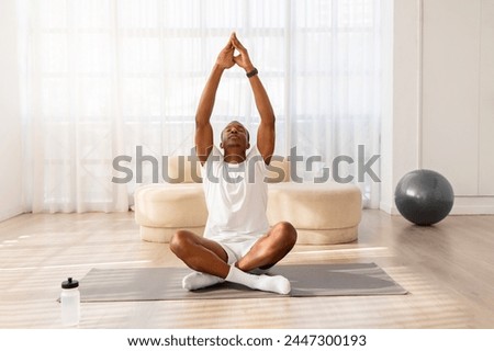 Tranquil African American man in comfortable athletic wear meditates on a yoga mat in a minimalist room Royalty-Free Stock Photo #2447300193