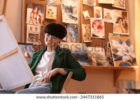 Portrait of smiling woman artist looking at picture in art studio or small business gallery, copy space