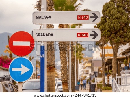 Spanish road sign pointing to Malaga and Granada on the highway N340. A "no entrance" sign is in the image as well. Palm trees and people in the background. Mediterranean coast, Andalusia.