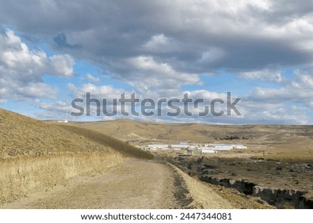 Photography of a road in a valley in an arid landscape whit a worker's village at the background