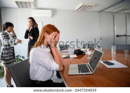 Two business women bully a colleague in the workplace, sad woman feels excluded. Royalty-Free Stock Photo #2447354019