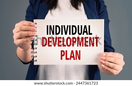 A woman holding a notepad with "individual development plan" written on it, on a gray background, stock photo