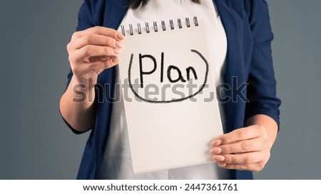 A woman holding a notepad with "plan" written on it, on a gray background, stock photo