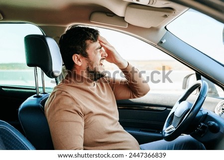 Young guy male with closed eyes, open mouth and beard. The driver sits in the car and suffers from headaches and neuralgia. Expressive facial expression. Royalty-Free Stock Photo #2447366839