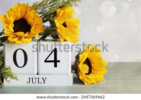 United States Independence Day. White wood calendar blocks with the date July 4th and beautiful sunflower bouquet with bokeh. Selective focus with blurred background. 