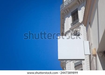 Selective blur on a Empty white square shop signboard hanging on a building facade, visible against a clear sky in a French city street ideal for retail business advertising  urban commercial display