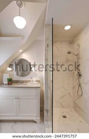 A modern bathroom with sleek tile shower, glass enclosure, chrome fixtures, and marble vanity. Pictured in a traditional cottage.