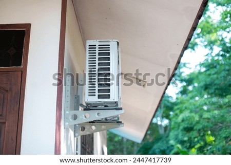 Air conditioner installed on the wall outside the house near the eaves of the house. Side photo.