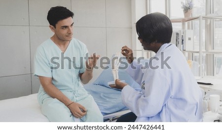Portrait patient caucasian man with woman nurse carer physical therapist African-American two people sitting talk helping support give advice and holding hand arm inside hospital indoor room service.