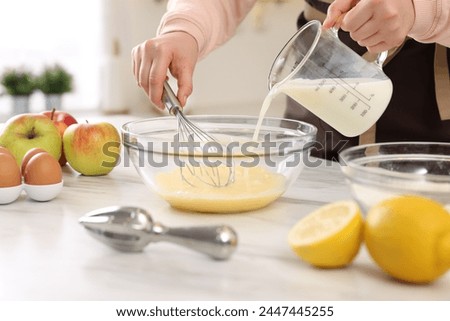 Woman whisking eggs while pouring milk into bowl at light marble table indoors, closeup Royalty-Free Stock Photo #2447445255