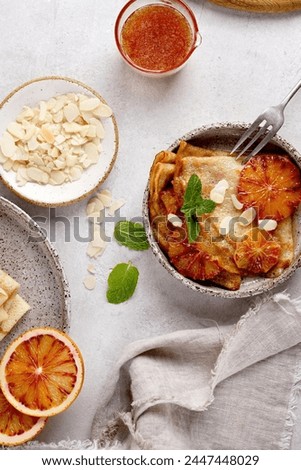 Crepes with Orange Sauce in a gray plate and almond petals, napkin, souce . Traditional French crepe Suzette with orange sauce. Flat lay, top view Royalty-Free Stock Photo #2447448029