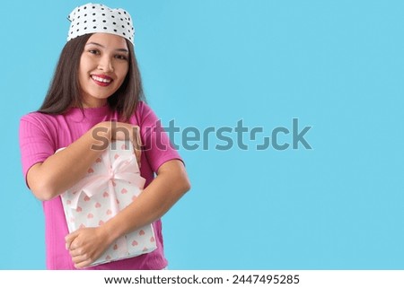 Beautiful young Asian woman with gift box on blue background