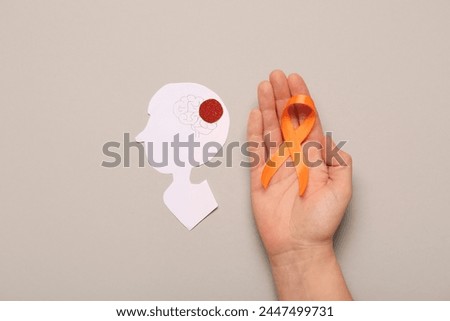 Female hand with orange ribbon and paper human head on grey background. Multiple Sclerosis Awareness Month Royalty-Free Stock Photo #2447499731