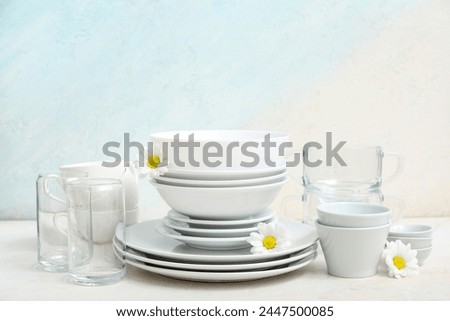 Composition with clean dishes, cups, glasses and beautiful chamomiles on table near light wall