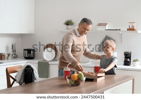 Mature doctor with his little son eating pizza in kitchen
