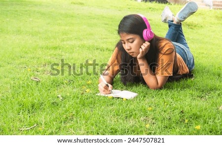 Girl enjoy listening music and reading a book and play laptop on the grass field of the park in the morning