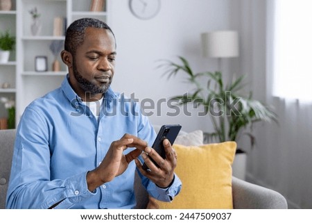Relaxed African American man browsing on phone while comfortably seated on a living room sofa.