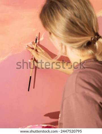 A woman, with long hair, is painting a pink wall with a brush