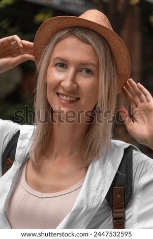 Cheerful and happy young female tourist in a hat. Portrait of a young beautiful smiling blonde woman in summer clothes. Carefree woman poses against the background of the street. Vertical photo