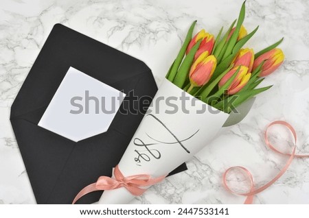Bouquet of tulips wrapped in paper with ribbon and blak sheet of paper to fill in with content. Black envelope. 
