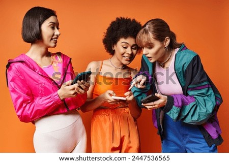 Three diverse women with different ethnicities standing next to each other, absorbed in their cell phones against an orange background. Royalty-Free Stock Photo #2447536565