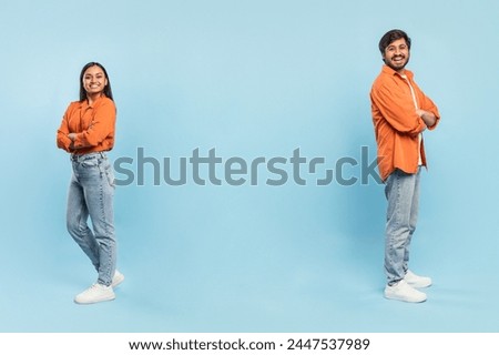 Confident Indian man and woman standing back-to-back with crossed arms in orange shirts and jeans, copy space Royalty-Free Stock Photo #2447537989