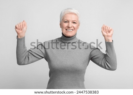 Cheerful senior european woman throws her fists up in a victory pose, ideal image for s3niorlife promotions Royalty-Free Stock Photo #2447538383