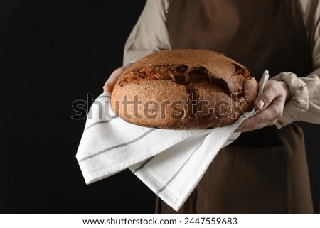Woman holding freshly baked bread on black background, closeup Royalty-Free Stock Photo #2447559683