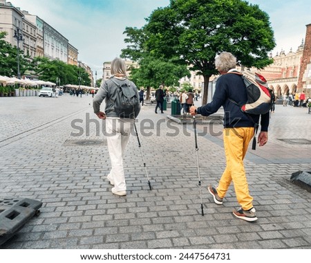 Two seniors enjoy urban exploration with walking sticks a tourist trip, showcasing active aging against a vibrant city square backdrop, perfect for lifestyle themes and happy aging Royalty-Free Stock Photo #2447564731