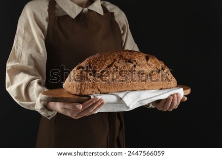 Woman holding freshly baked bread on black background, closeup Royalty-Free Stock Photo #2447566059
