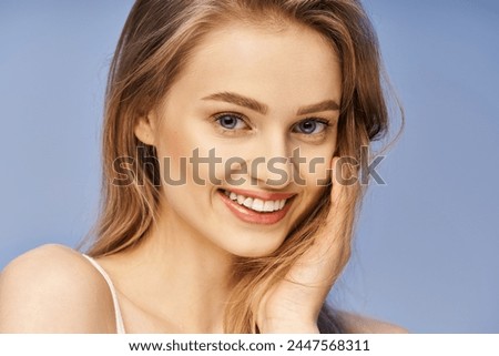 A young, beautiful woman with blonde hair striking a pose, smiling happily for a professional photoshoot in a studio setting.