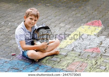 Little active kid boy drawing knight castle and fortress with colorful chalks on asphalt. Happy child with big helmet having fun with playing knight game and painting