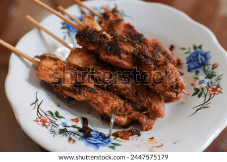 Several skewers of chicken meat in a white plate on a wooden table, traditional meal, Indonesian food, stock photo.