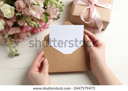 Happy Mother's Day. Woman holding envelope with blank card at white wooden table, top view