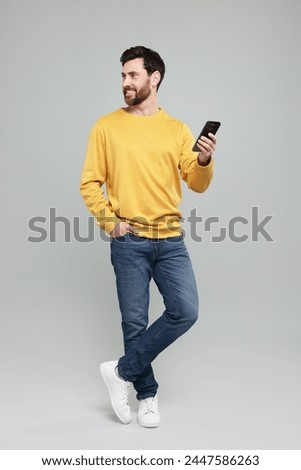 Smiling man with smartphone on grey background