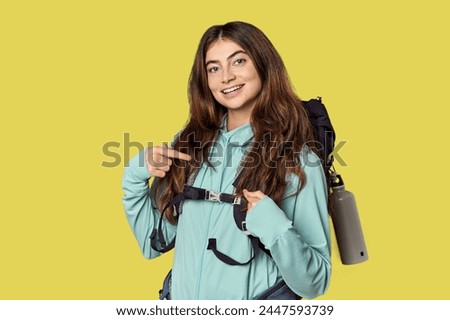 Young Caucasian woman with mountain backpack person pointing by hand to a shirt copy space, proud and confident
