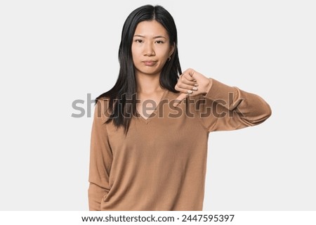 Young Chinese woman in studio setting showing thumb down, disappointment concept.