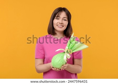 Easter celebration. Happy woman with wrapped egg on orange background