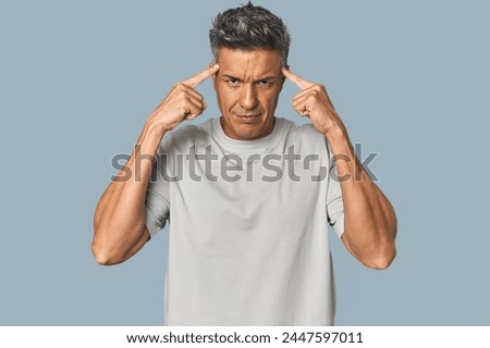Middle-aged Latino man focused on a task, keeping forefingers pointing head.