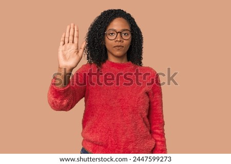 African American woman in studio setting standing with outstretched hand showing stop sign, preventing you.