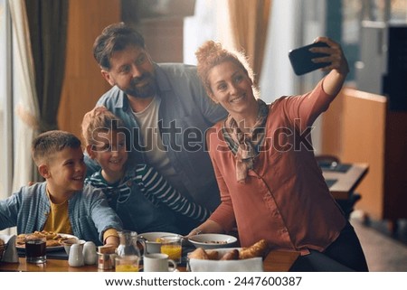 Happy woman taking selfie with her family while eating breakfast in a restaurant.