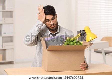 Unemployment problem. Frustrated man with box of personal belongings at desk in office Royalty-Free Stock Photo #2447600725