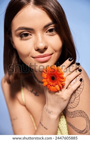 A young woman with brunette hair holding a vibrant flower in her hand, showcasing natural beauty and grace.