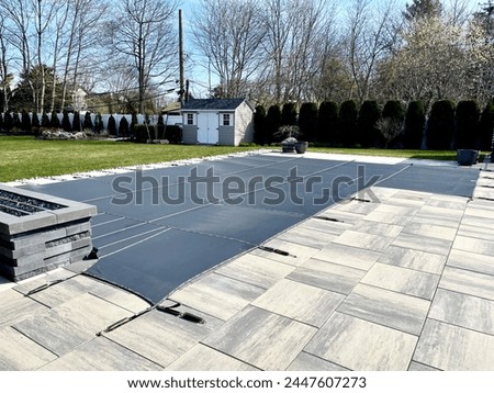 Winterized L-shaped built-in, inground pool with safety Loop - Loc mesh cover to protect it.  Allows melting snow and rain to drain through it. Brass anchors are flush to the paver height.   Royalty-Free Stock Photo #2447607273