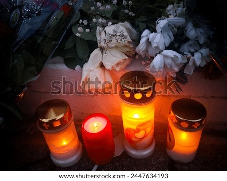 Memorial burning candle with glowing flame inside framed by other blurry candles and flowers put in memory of victims of terrorist attack in evening. Image of tribute to killed innocent victims Royalty-Free Stock Photo #2447634193