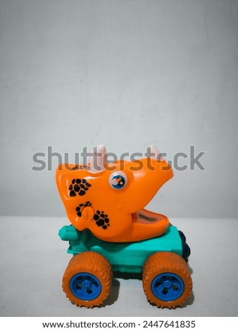 The dinosaur car is orange, a combination of light blue, dark blue and black, has 4 wheels. Toys for children aged over 2 years. The mouth is open and has horns