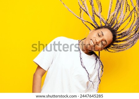 young african american woman with dreadlocks waving her head and dancing on yellow isolated background, girl with unique hairstyle and colored braids hair flying